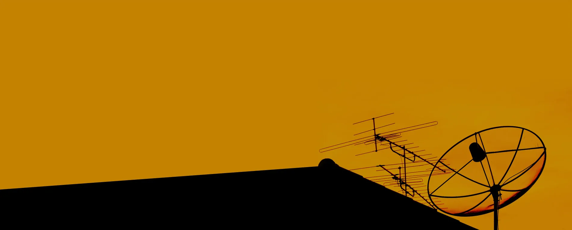 Antenna and satellite dish silhouetted on a roof