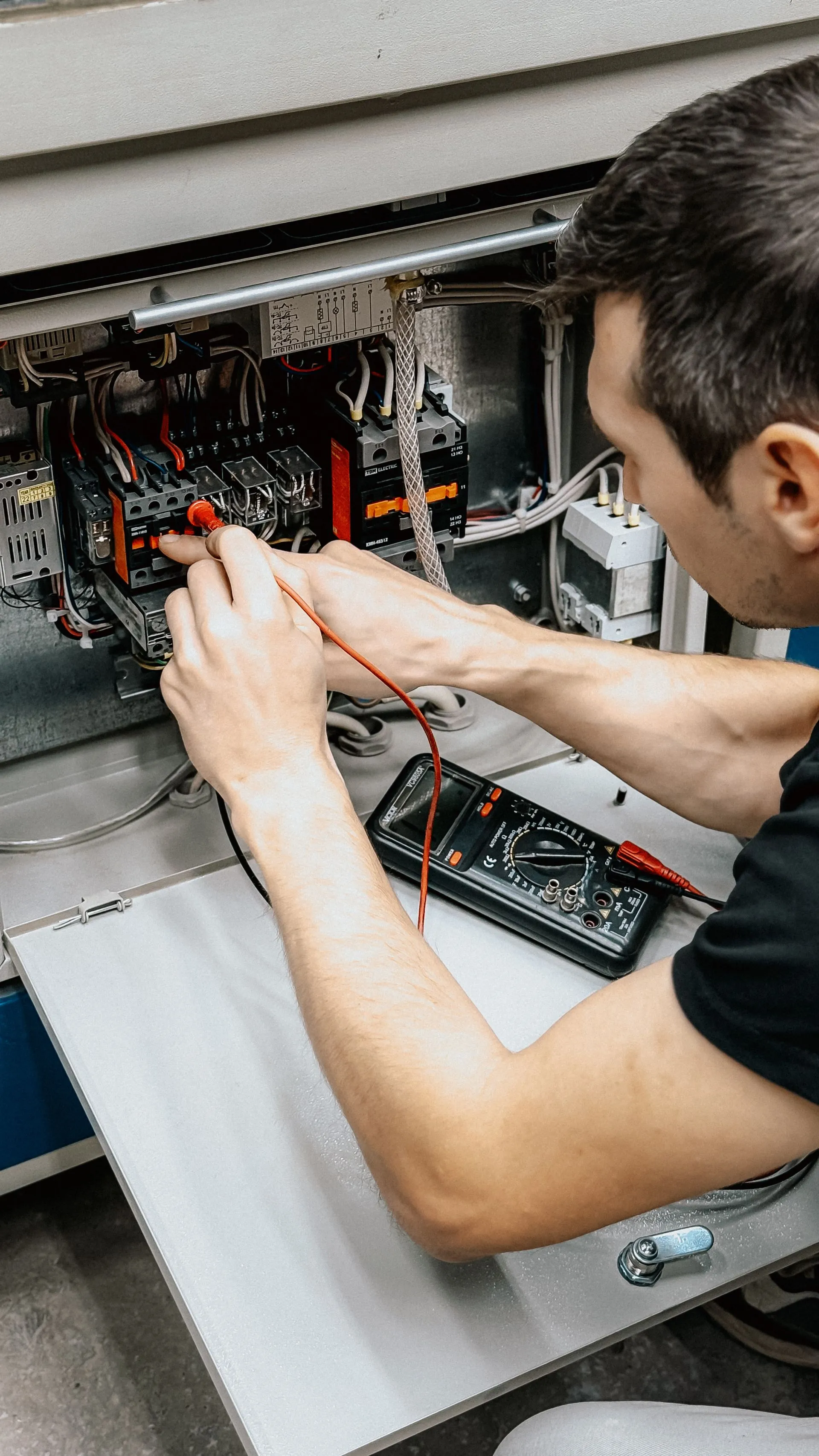 Technician testing wiring inside an electrical panel with a multimeter