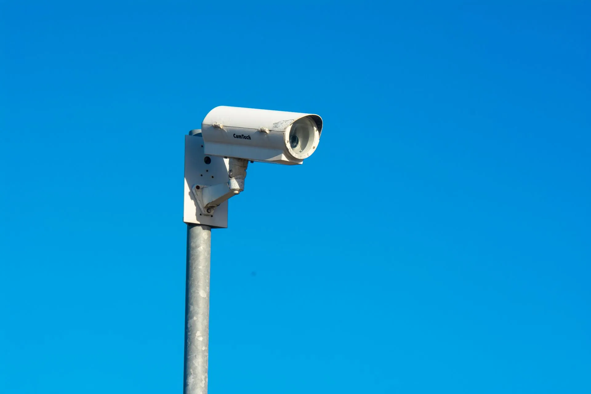 White CCTV security camera mounted on a pole against a clear blue sky